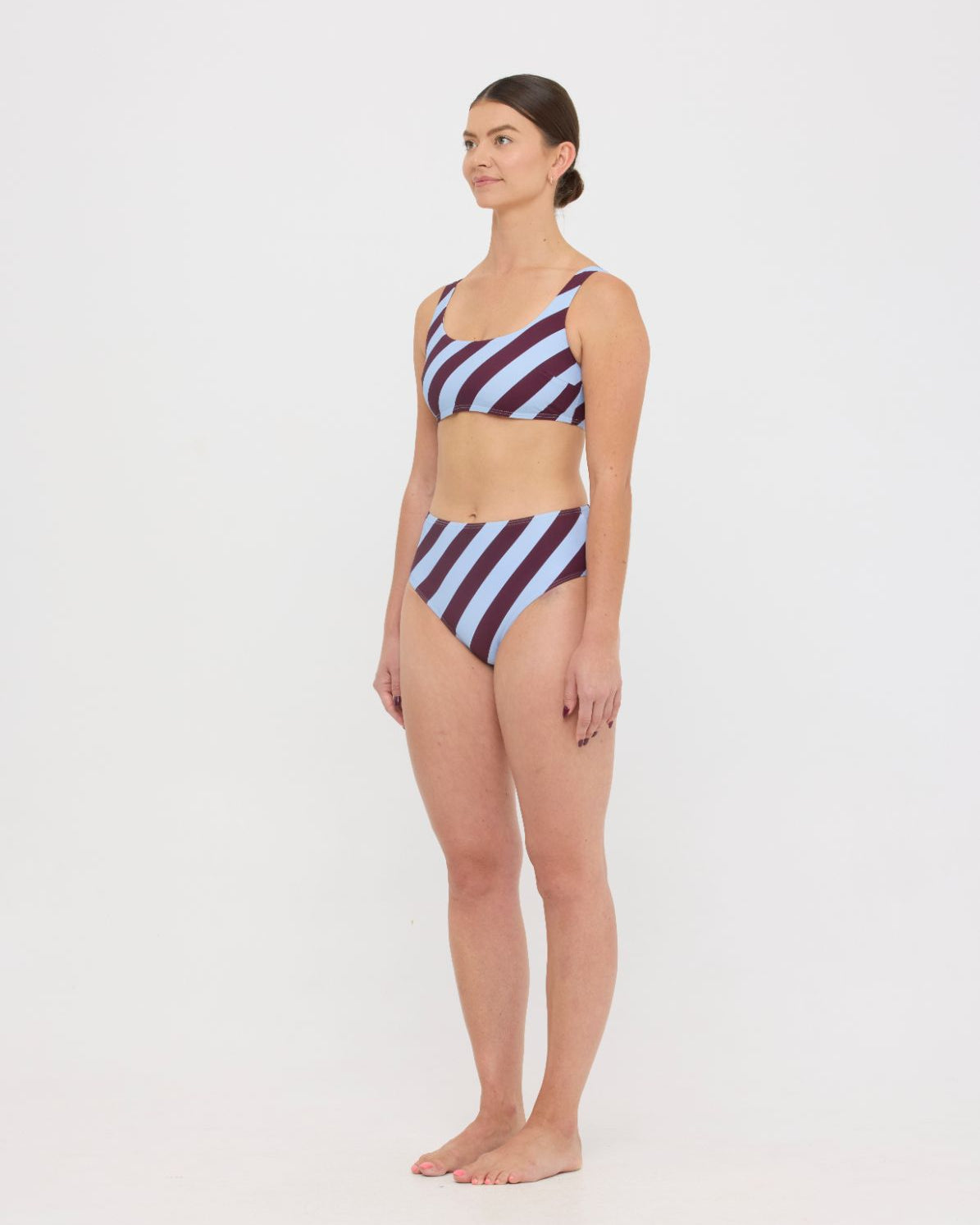 Woman wearing dusty blue and plum rising-stripe HUZZAH Chilli crop top with high-waisted full-coverage bikini bottoms on white background.