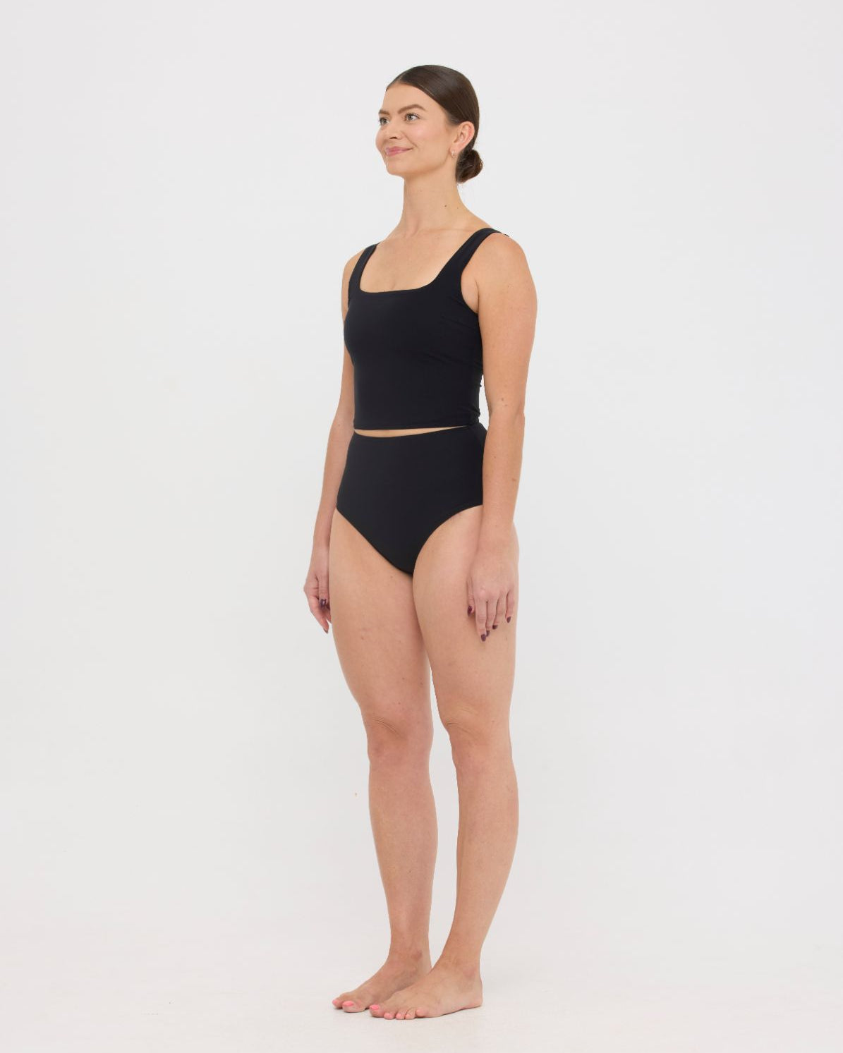 Woman wearing black HUZZAH Ted tank top with high-waisted full-coverage bikini bottoms on white background.