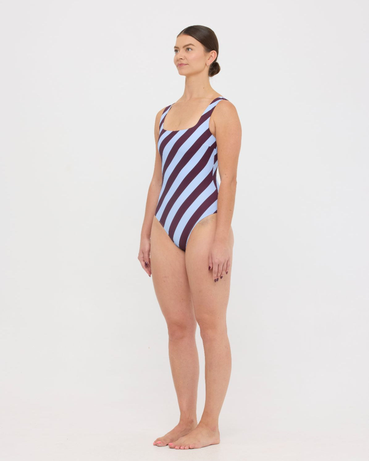 Model wearing the dusty blue and plum rising stripe HUZZAH Cat one-piece swimsuit with sculpting fit and clean lines, photographed against a plain background