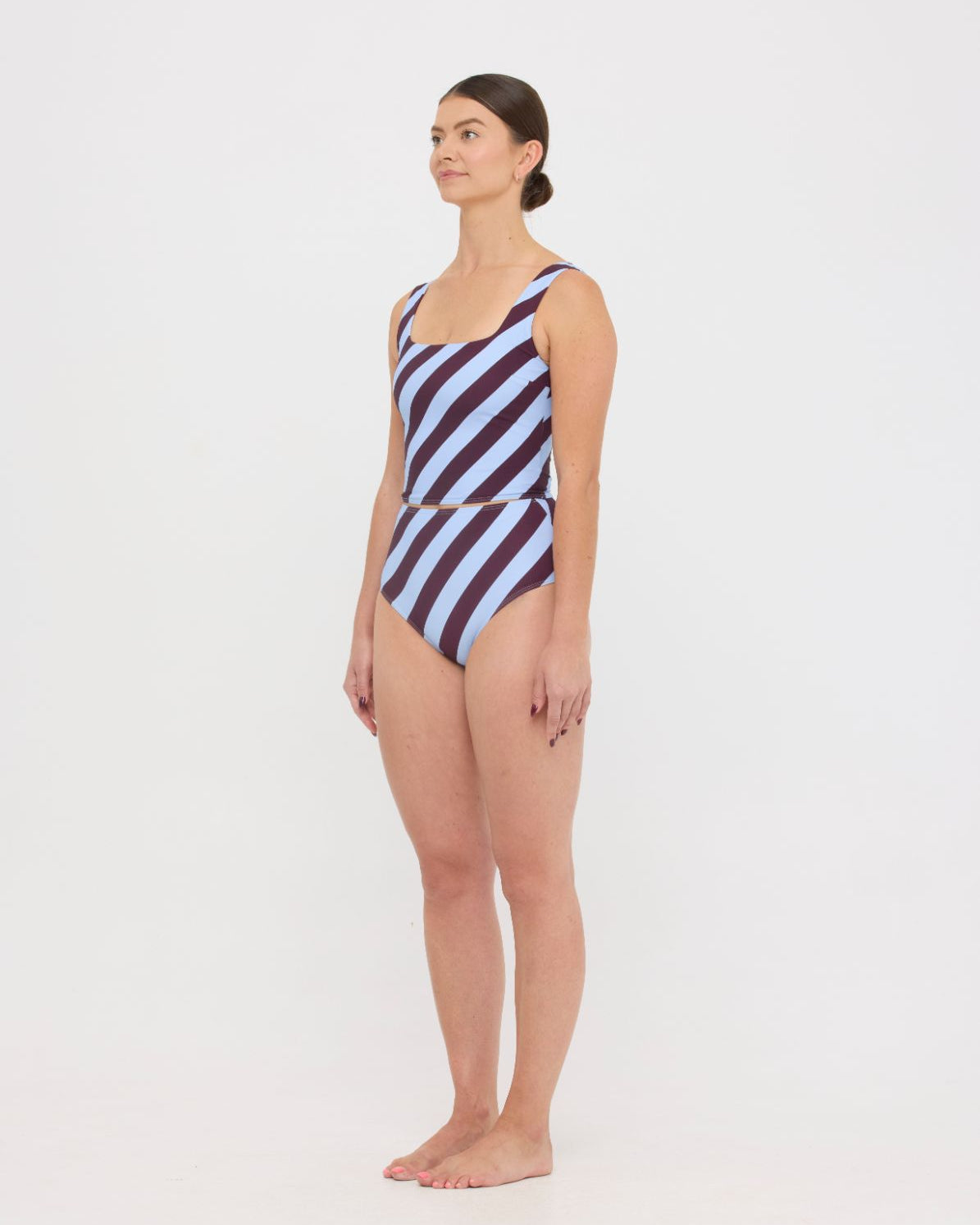 Woman wearing dusty blue and plum rising-stripe HUZZAH Ted tank top with high-waisted full-coverage bikini bottoms on white background.