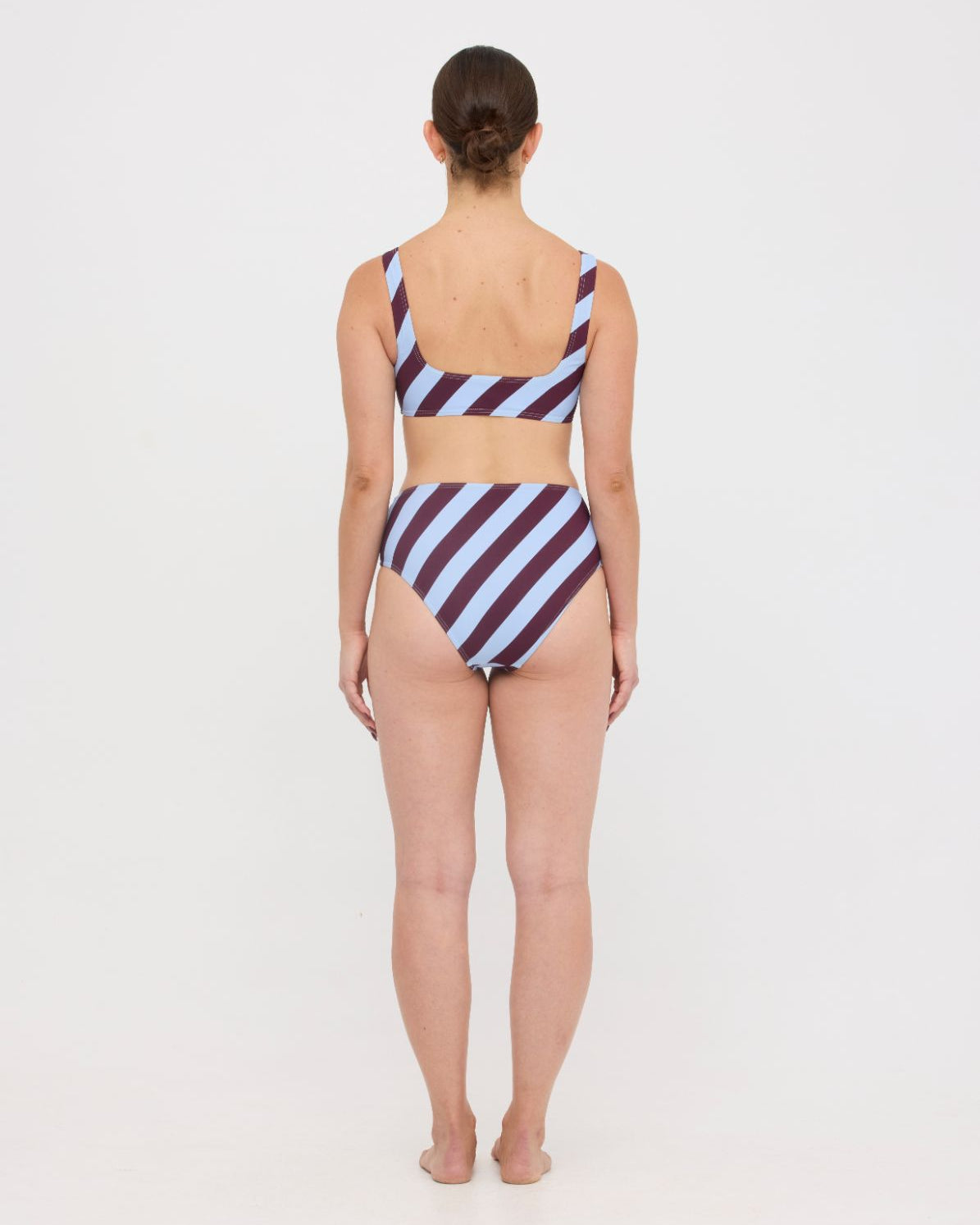 Woman wearing dusty blue and plum rising-stripe HUZZAH Chilli crop top with high-waisted full-coverage bikini bottoms on white background.