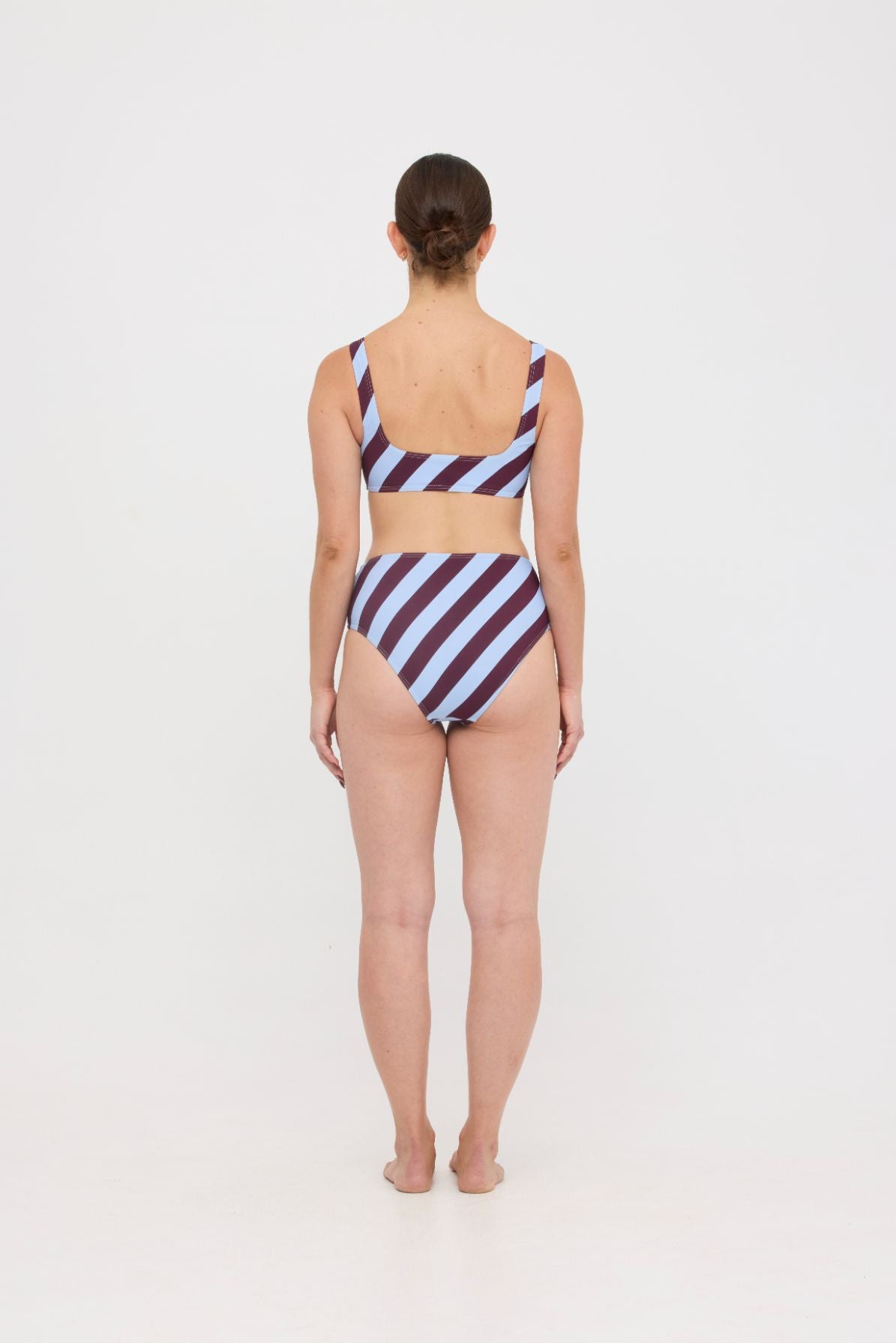 Woman wearing dusty blue and plum rising-stripe HUZZAH Chilli crop top with high-waisted full-coverage bikini bottoms on white background.