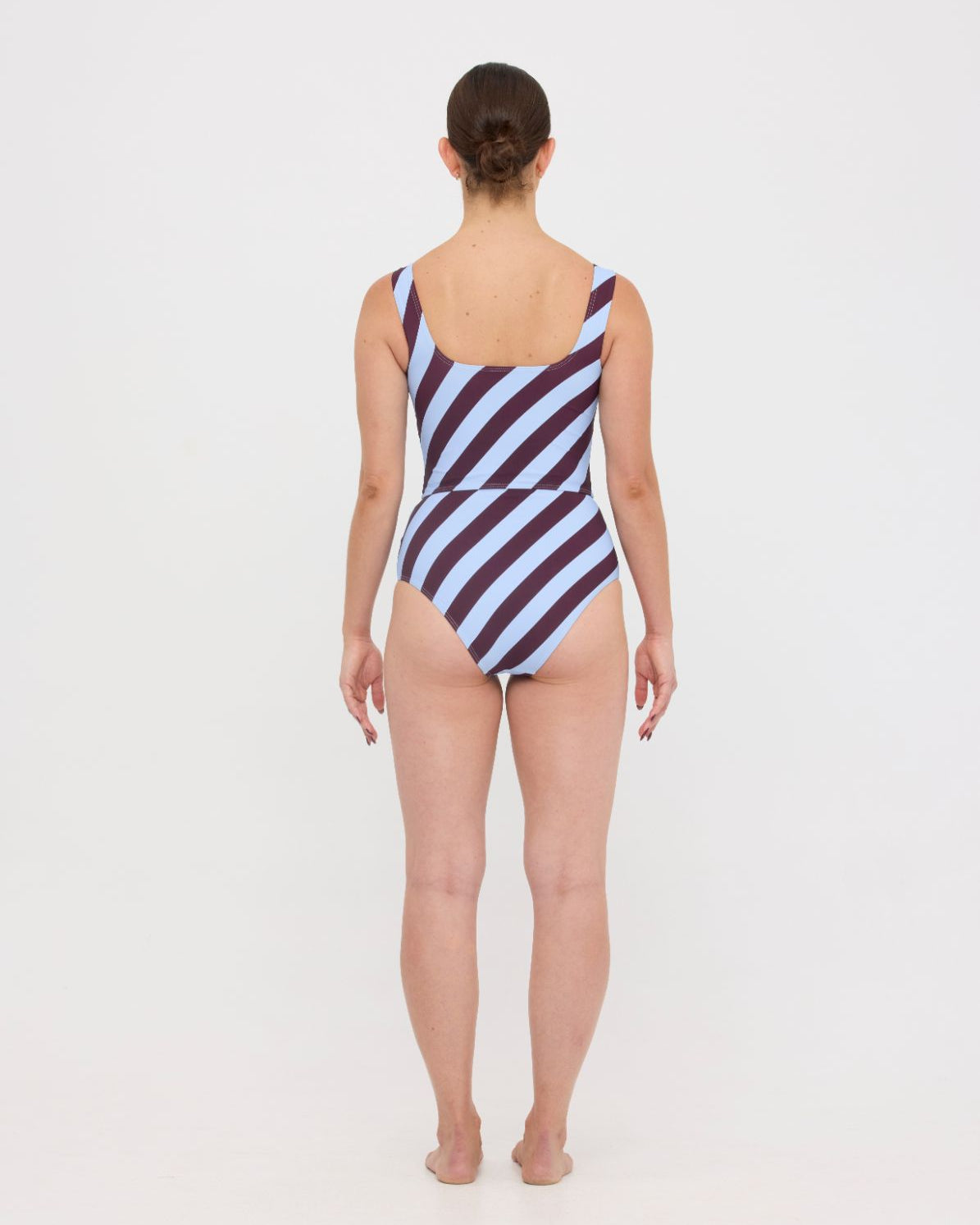 Woman wearing dusty blue and plum rising-stripe HUZZAH Ted tank top with high-waisted full-coverage bikini bottoms on white background.