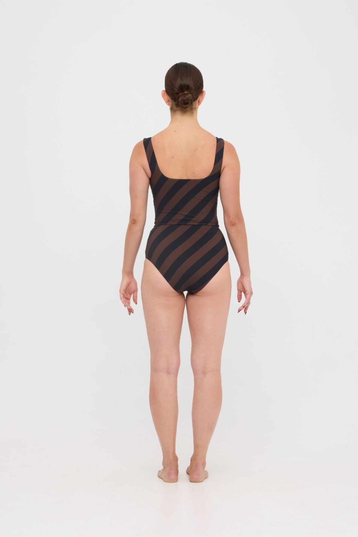 Woman wearing espresso and black rising stripe HUZZAH Ted tank top with high-waisted full-coverage bikini bottoms on white background.