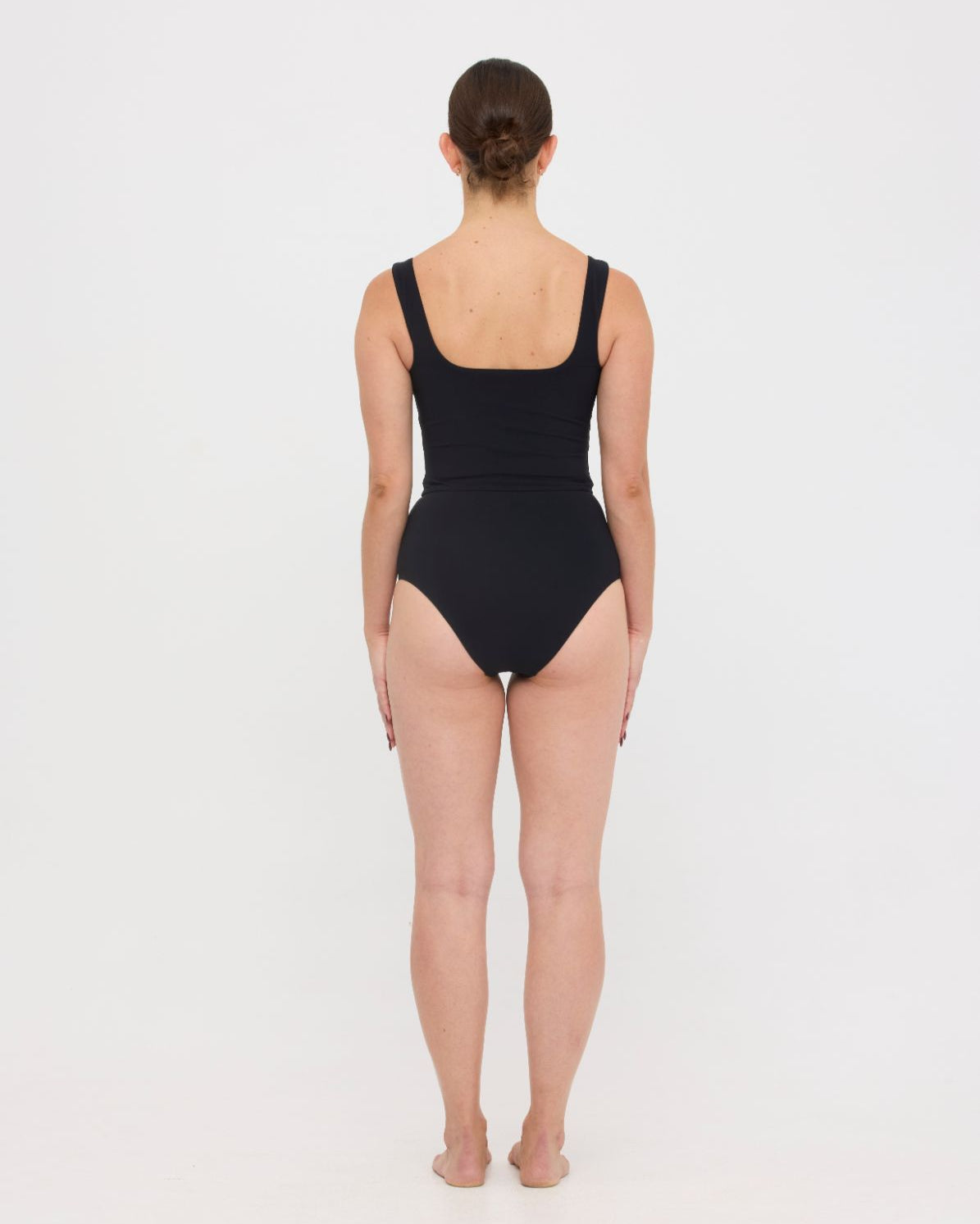 Woman wearing black HUZZAH Ted tank top with high-waisted full-coverage bikini bottoms on white background.