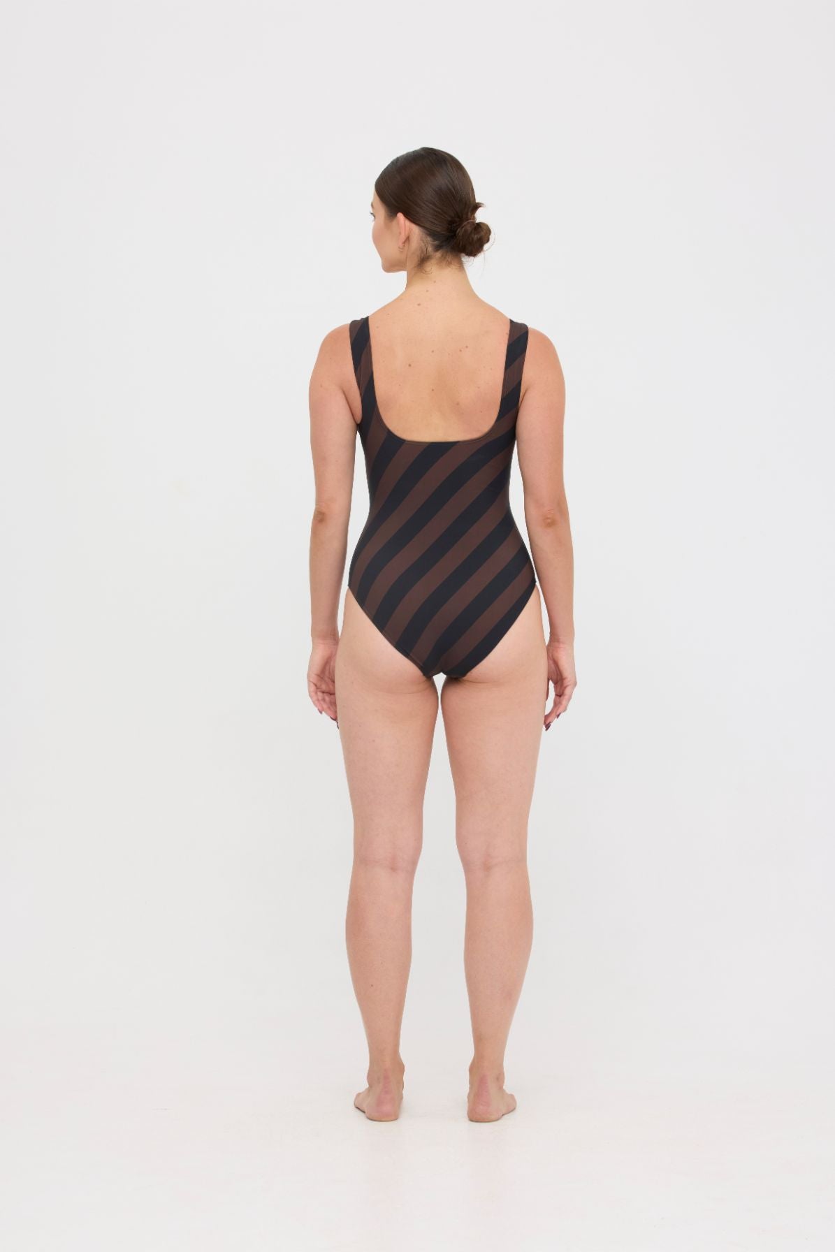 Model wearing the espresso and black rising stripe HUZZAH Cat one-piece swimsuit with sculpting fit and clean lines, photographed against a plain background