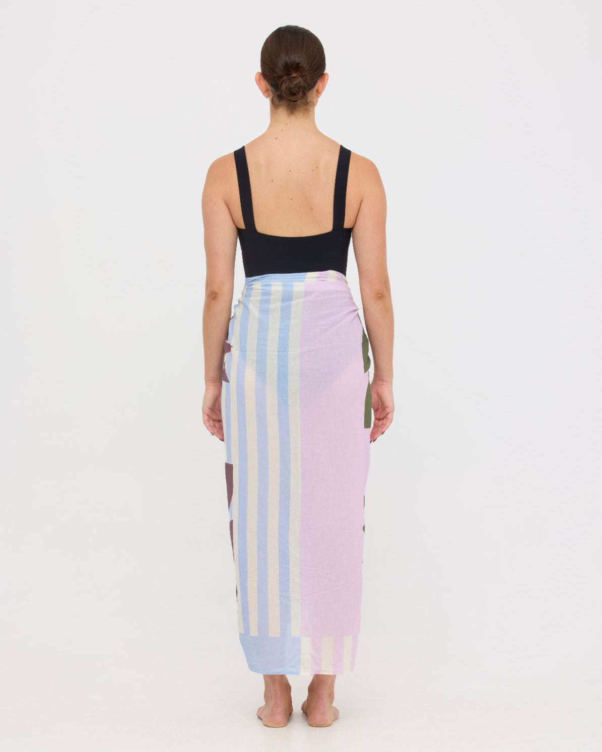 Woman wearing the black HUZZAH Scout sculpting one-piece with a lightweight multi coloured sarong wrapped at the hip, creating a sophisticated swimwear look.