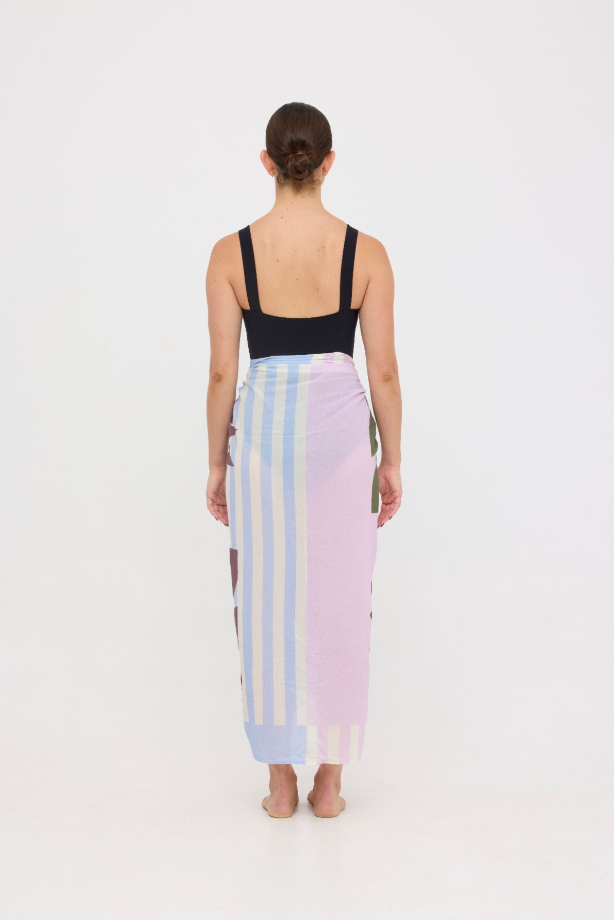 Woman wearing the black HUZZAH Scout sculpting one-piece with a lightweight multi coloured sarong wrapped at the hip, creating a sophisticated swimwear look.