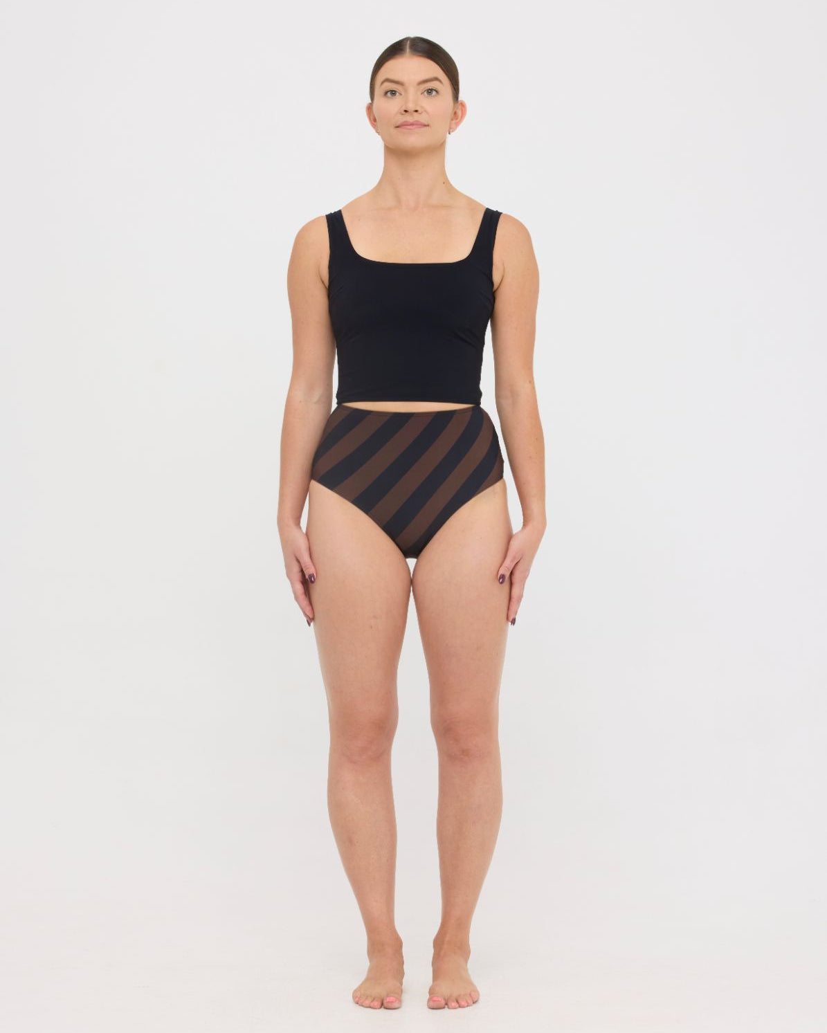 Model in black sculpting HUZZAH Ted tank and espresso and black rising stripe high-waisted full-coverage bikini bottoms against white background.