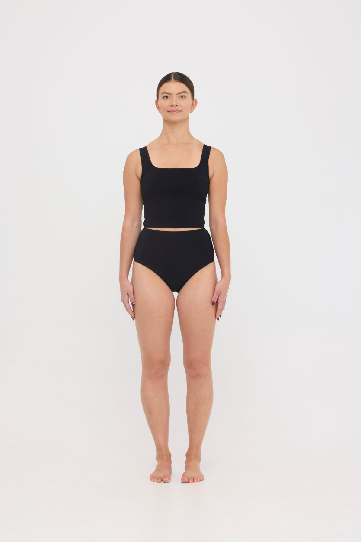 Woman wearing black HUZZAH Ted tank top with high-waisted full-coverage bikini bottoms on white background.