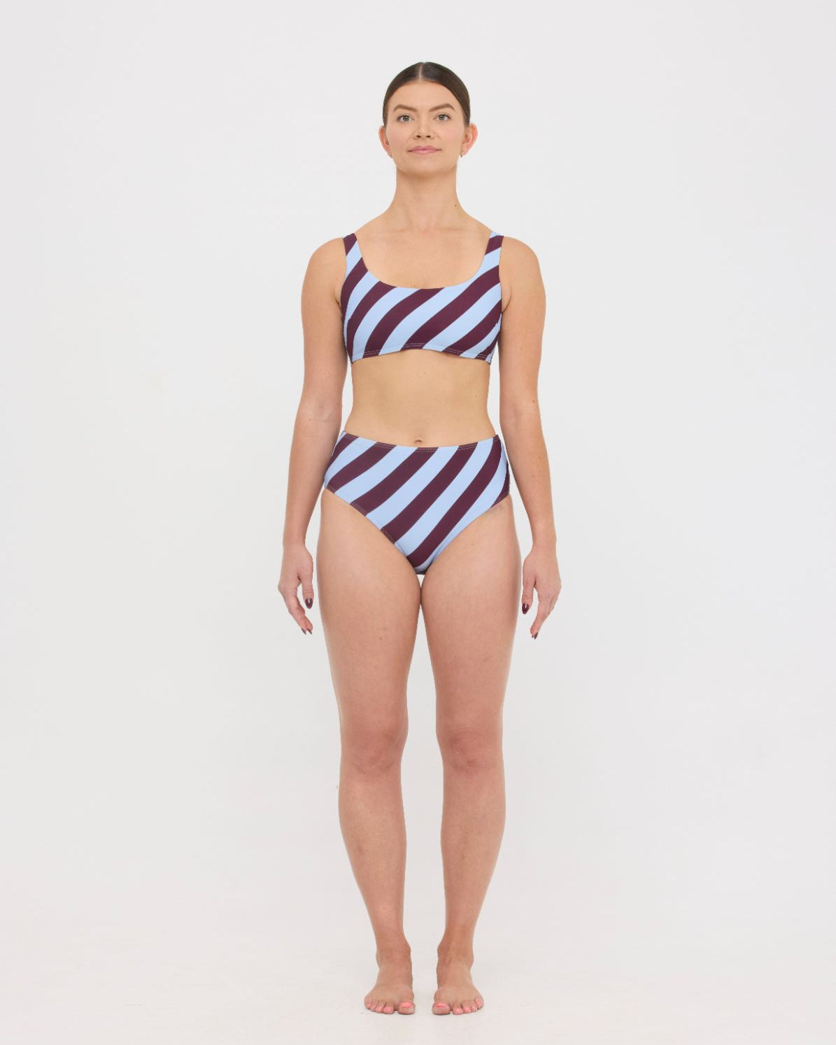 Woman wearing dusty blue and plum rising-stripe HUZZAH Chilli crop top with high-waisted full-coverage bikini bottoms on white background.