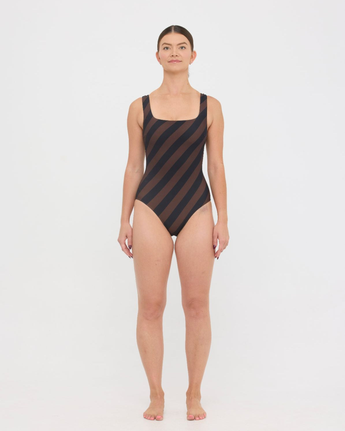 Model wearing the espresso and black rising stripe HUZZAH Cat one-piece swimsuit with sculpting fit and clean lines, photographed against a plain background