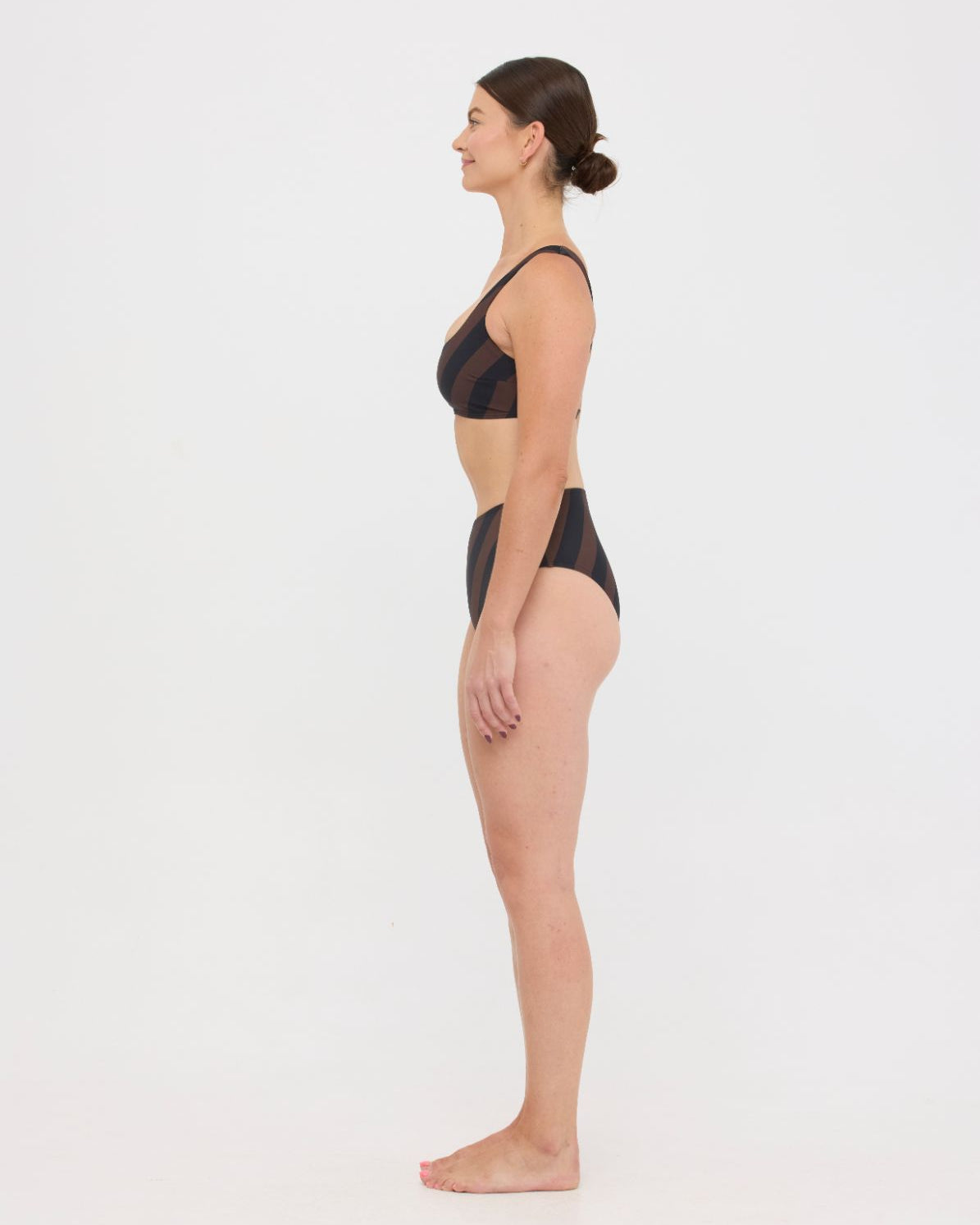 Woman wearing espresso and black rising-stripe HUZZAH Chilli crop top with high-waisted full-coverage bikini bottoms on white background.