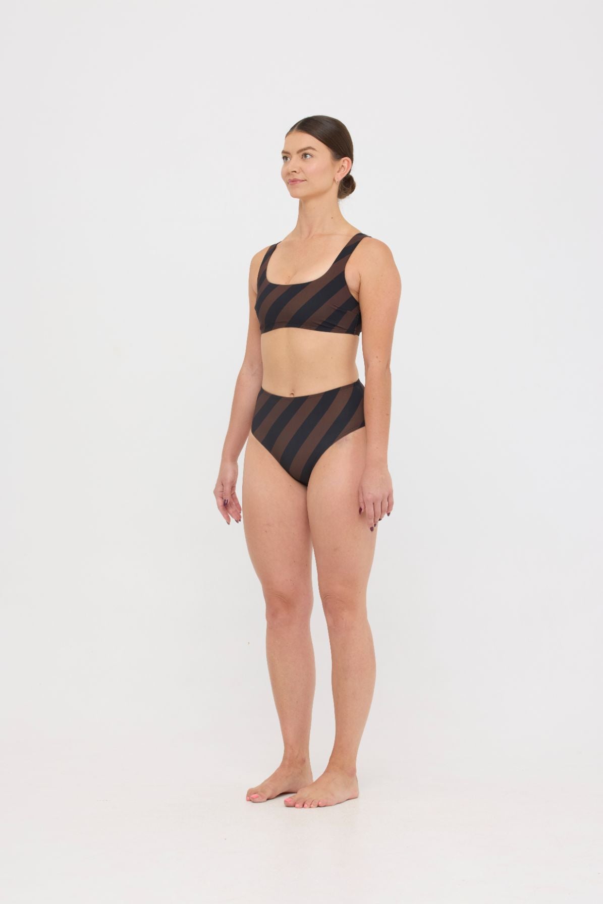 Woman wearing espresso and black rising-stripe HUZZAH Chilli crop top with high-waisted full-coverage bikini bottoms on white background.