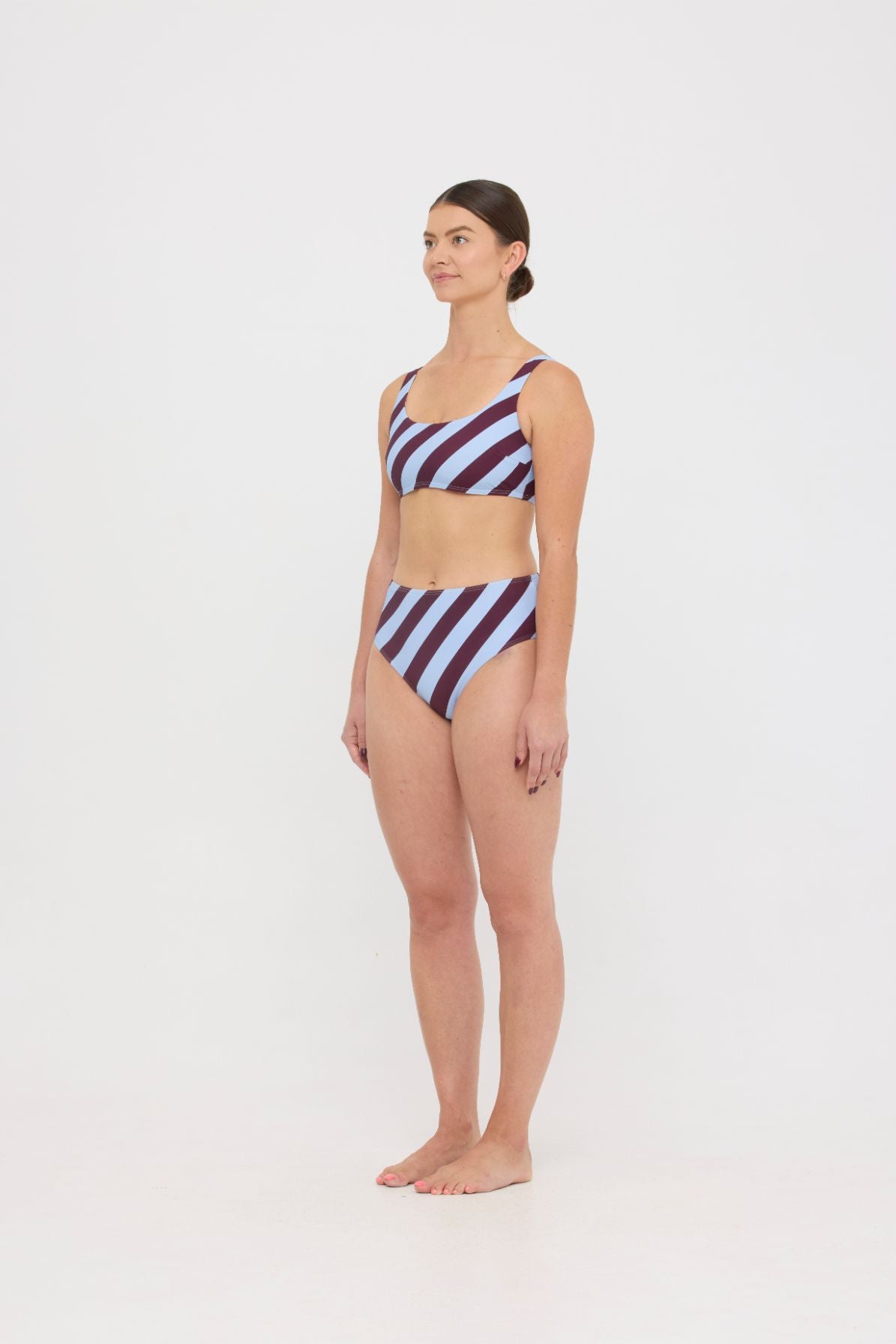 Woman wearing dusty blue and plum rising-stripe HUZZAH Chilli crop top with high-waisted full-coverage bikini bottoms on white background.