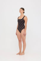 Model wearing the espresso and black rising stripe HUZZAH Cat one-piece swimsuit with sculpting fit and clean lines, photographed against a plain background