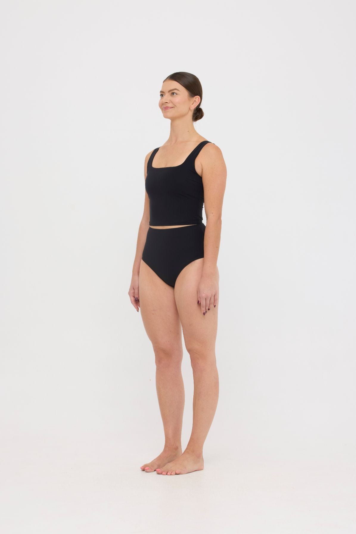 Woman wearing black HUZZAH Ted tank top with high-waisted full-coverage bikini bottoms on white background.