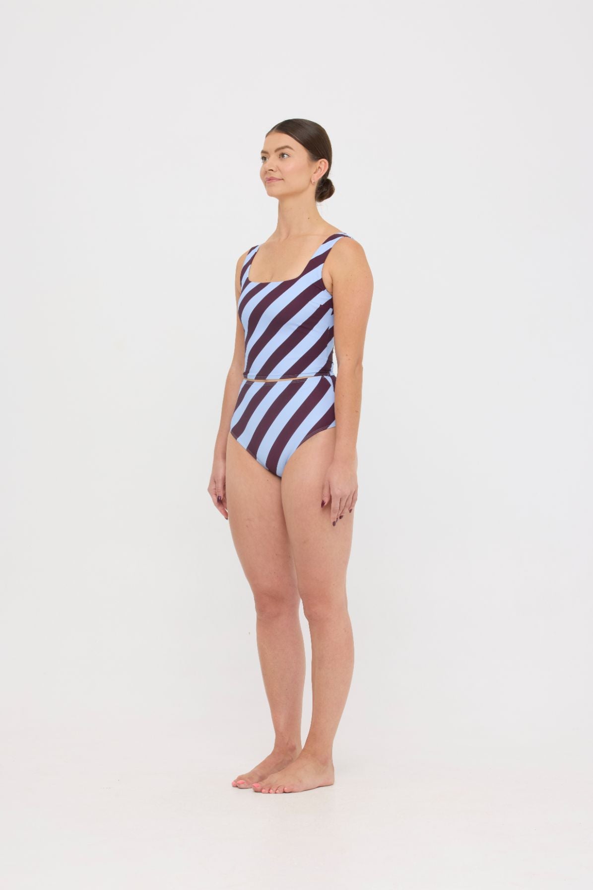 Woman wearing dusty blue and plum rising-stripe HUZZAH Ted tank top with high-waisted full-coverage bikini bottoms on white background.