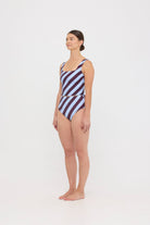 Woman wearing dusty blue and plum rising-stripe HUZZAH Ted tank top with high-waisted full-coverage bikini bottoms on white background.