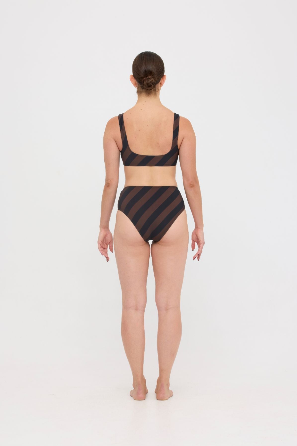 Woman wearing espresso and black rising-stripe HUZZAH Chilli crop top with high-waisted full-coverage bikini bottoms on white background.