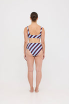 Woman wearing dusty blue and plum rising-stripe HUZZAH Chilli crop top with high-waisted full-coverage bikini bottoms on white background.
