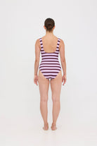 Model wearing the violet and plum mixed stripe HUZZAH Cat one-piece swimsuit with sculpting fit and clean lines, photographed against a plain background