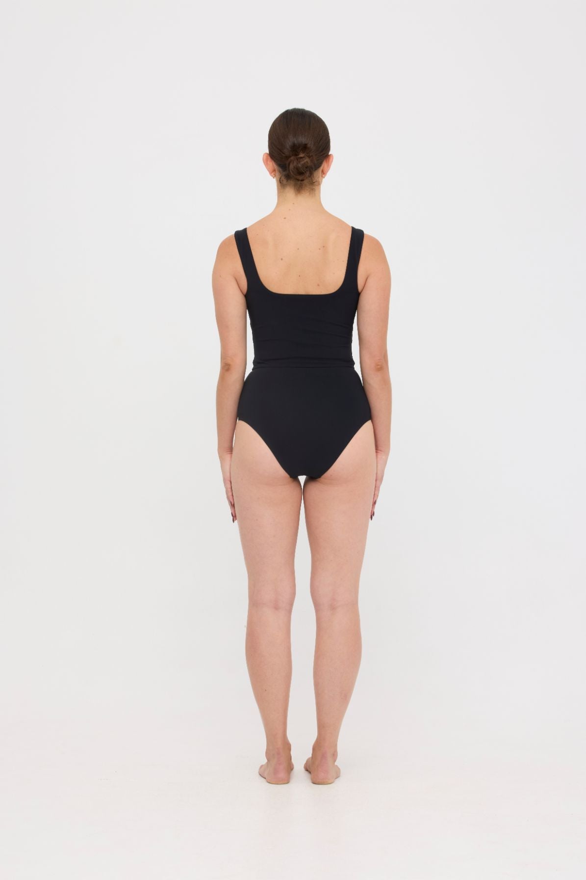 Woman wearing black HUZZAH Ted tank top with high-waisted full-coverage bikini bottoms on white background.