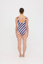 Model wearing the dusty blue and plum rising stripe HUZZAH Cat one-piece swimsuit with sculpting fit and clean lines, photographed against a plain background