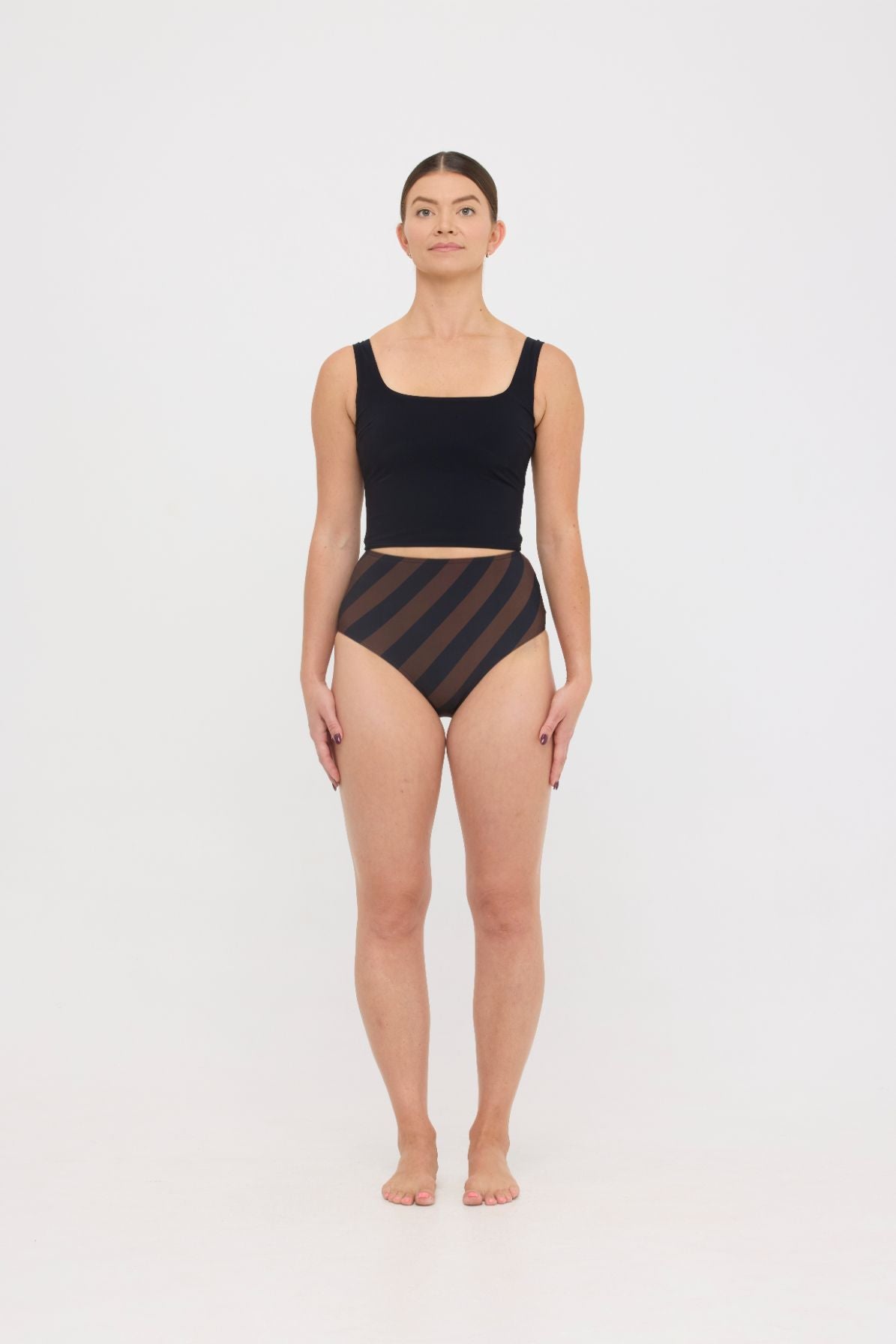 Model in black sculpting HUZZAH Ted tank and espresso and black rising stripe high-waisted full-coverage bikini bottoms against white background.