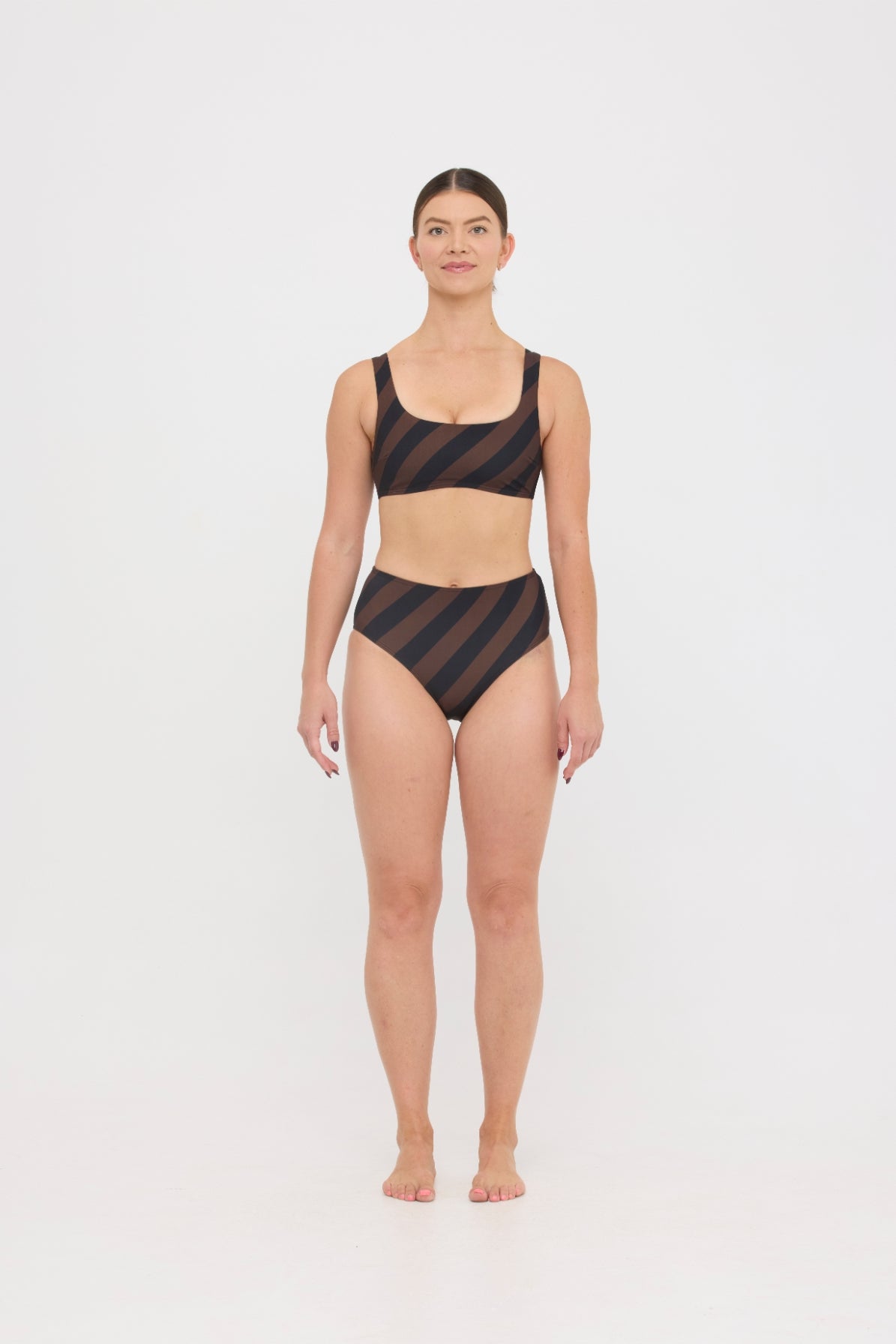 Woman wearing espresso and black rising-stripe HUZZAH Chilli crop top with high-waisted full-coverage bikini bottoms on white background.