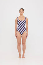 Model wearing the dusty blue and plum rising stripe HUZZAH Cat one-piece swimsuit with sculpting fit and clean lines, photographed against a plain background