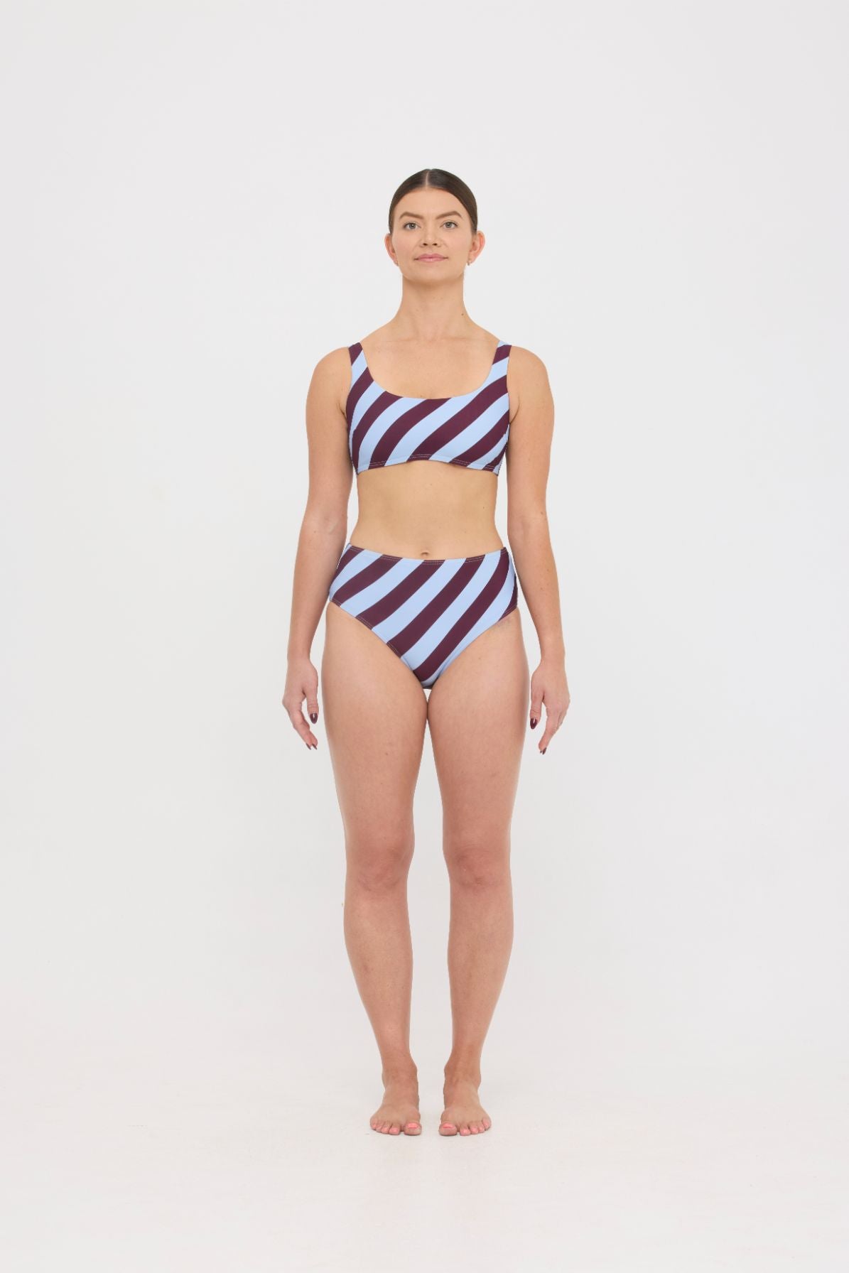 Woman wearing dusty blue and plum rising-stripe HUZZAH Chilli crop top with high-waisted full-coverage bikini bottoms on white background.