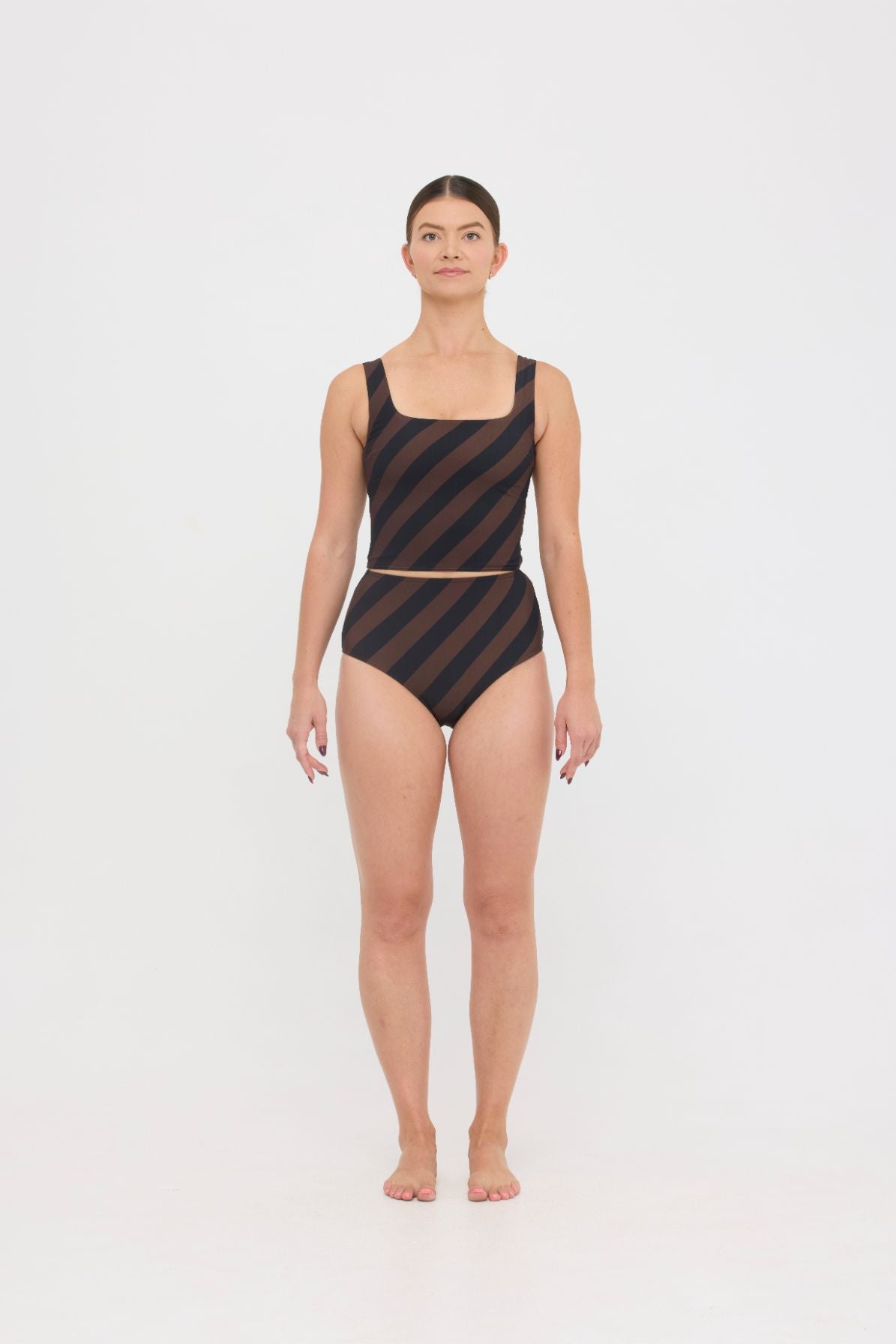 Woman wearing espresso and black rising stripe HUZZAH Ted tank top with high-waisted full-coverage bikini bottoms on white background.