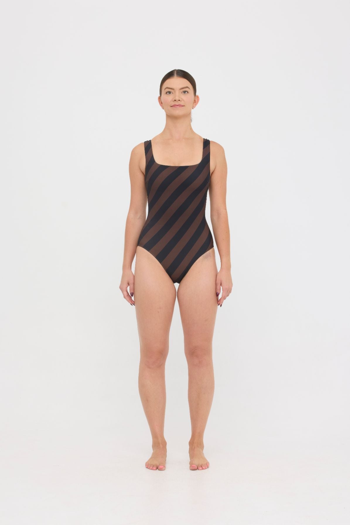 Model wearing the espresso and black rising stripe HUZZAH Cat one-piece swimsuit with sculpting fit and clean lines, photographed against a plain background