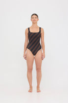 Model wearing the espresso and black rising stripe HUZZAH Cat one-piece swimsuit with sculpting fit and clean lines, photographed against a plain background