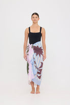 Woman wearing the black HUZZAH Scout sculpting one-piece with a lightweight multi coloured sarong wrapped at the hip, creating a sophisticated swimwear look.