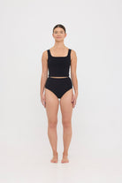 Woman wearing black HUZZAH Ted tank top with high-waisted full-coverage bikini bottoms on white background.