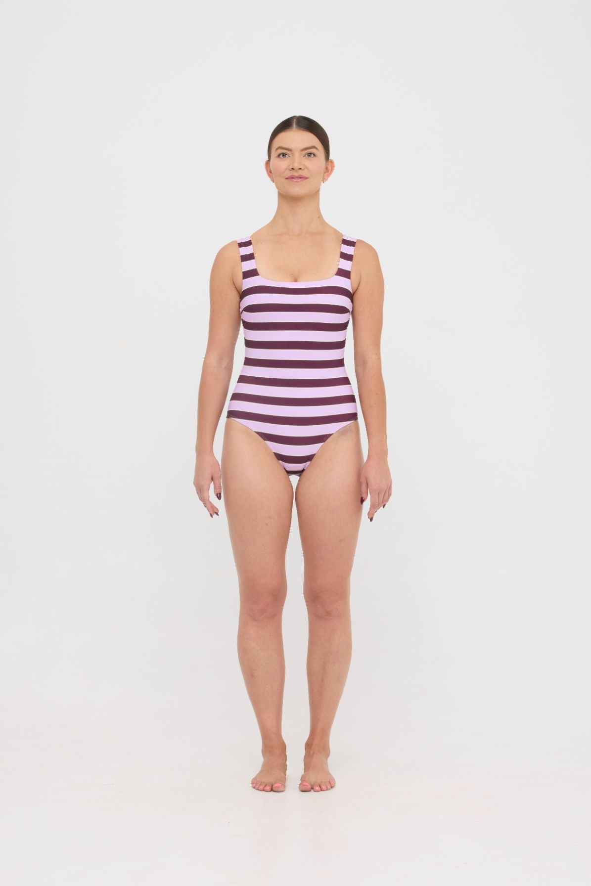 Model wearing the violet and plum mixed stripe HUZZAH Cat one-piece swimsuit with sculpting fit and clean lines, photographed against a plain background