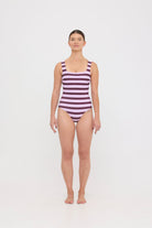 Model wearing the violet and plum mixed stripe HUZZAH Cat one-piece swimsuit with sculpting fit and clean lines, photographed against a plain background