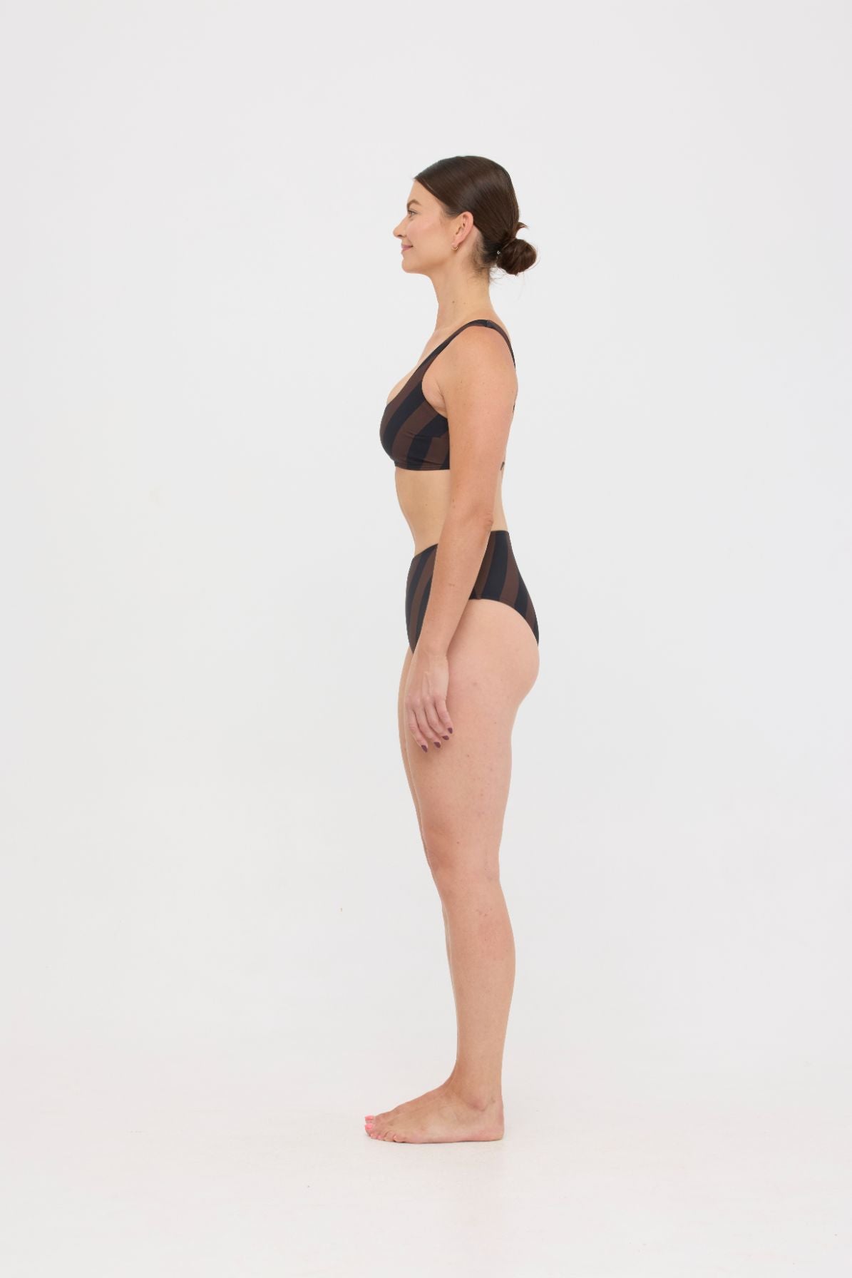 Woman wearing espresso and black rising-stripe HUZZAH Chilli crop top with high-waisted full-coverage bikini bottoms on white background.