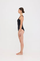 Model wearing the black HUZZAH Scout one-piece swimsuit with sculpting fit and clean lines, photographed against a plain background