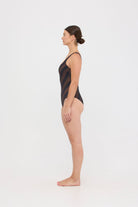 Model wearing the espresso and black rising stripe HUZZAH Cat one-piece swimsuit with sculpting fit and clean lines, photographed against a plain background
