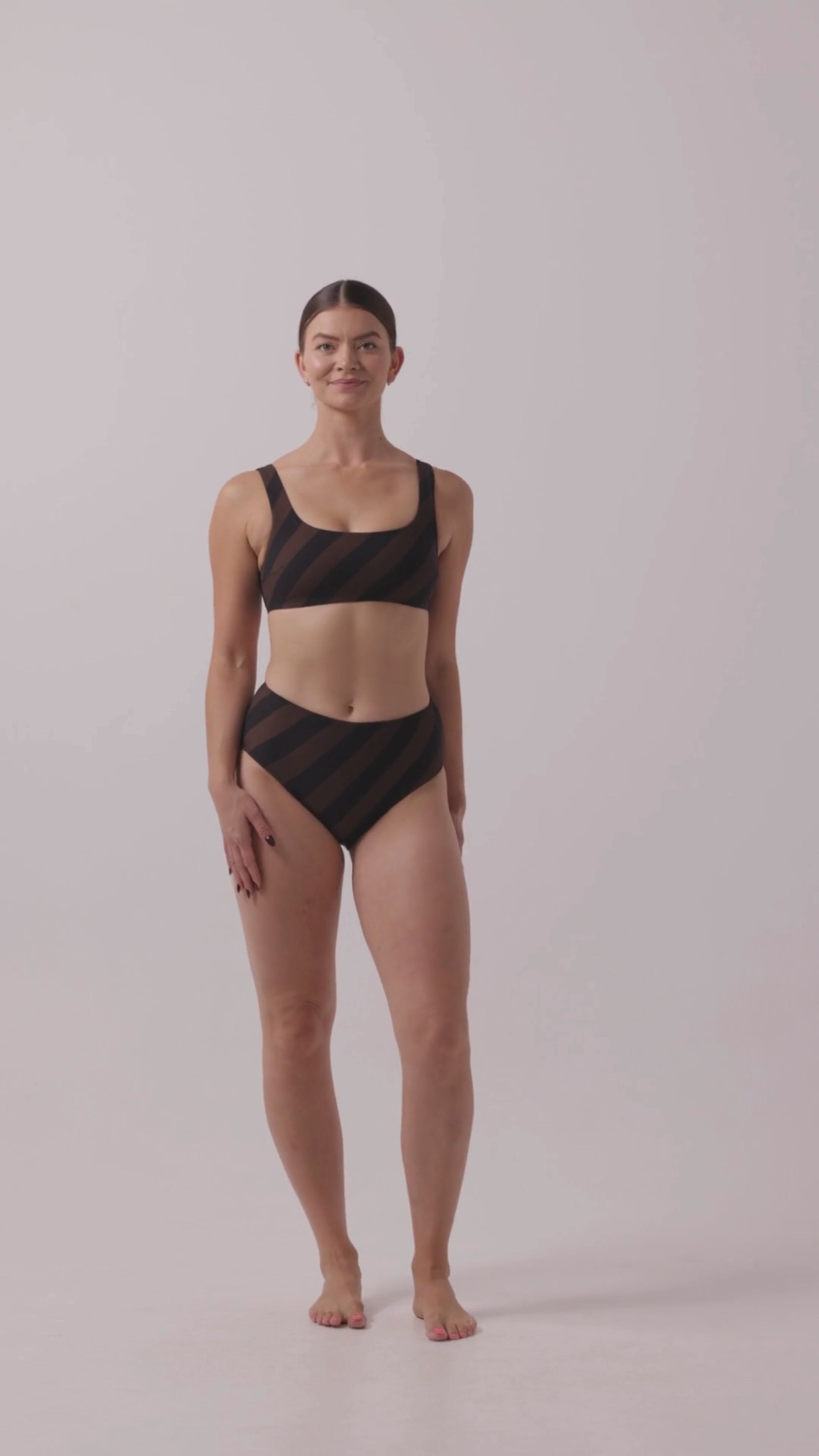 Model in espresso and black rising stripe HUZZAH Chilli crop bikini top paired with mid-waisted full-coverage bottoms